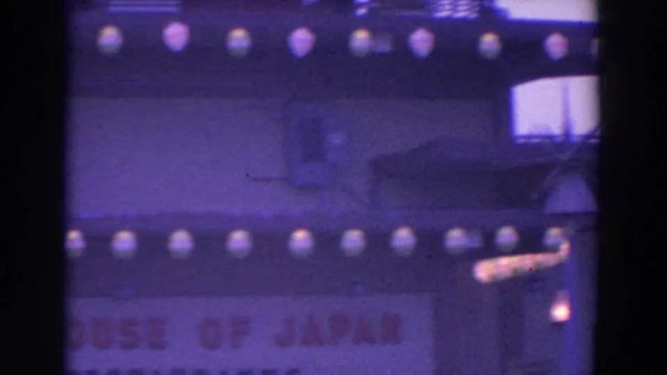 1964 World's Fair 8mm frame showing the lower House of Japan facade with globe lights and partially cropped red lettering.