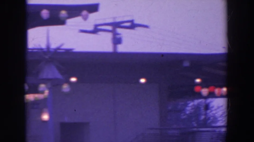 Nighttime 8mm view of the House of Japan pavilion area, showing a pale wall, sign support, globe lights, and deep shadows.