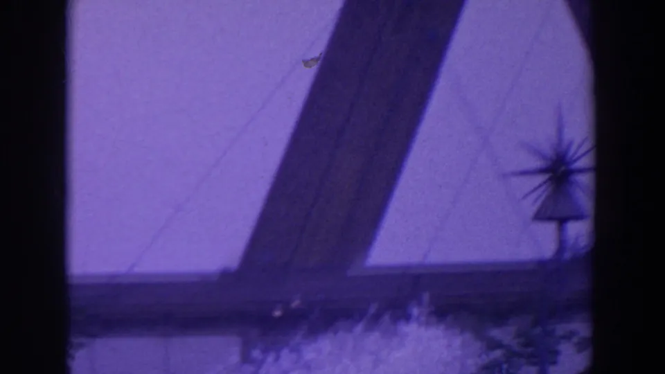 The camera shifts downward to a pale facade and dark diagonal forms, with a small spiky ornament silhouetted near the lower center.