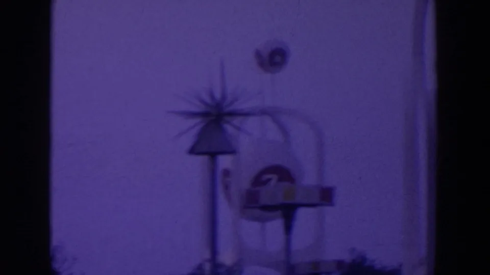 Nighttime fair view with a starburst pylon and round sign or emblem shape near a pavilion, tinted purple by the film scan.