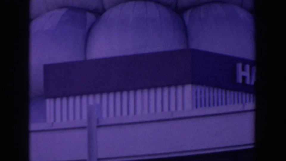 A handheld 8mm frame shows a purple-tinted hall exterior with a partial sign, arched facade details, and railing-like trim.