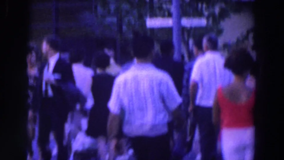 Visitors walk through a crowded outdoor fairground path, seen from behind in soft, grainy 8mm color.