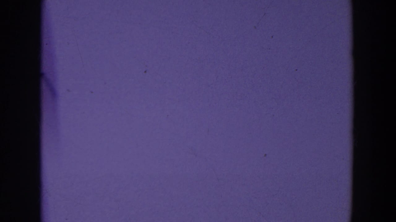Purple-tinted sky-like frame with a dark vertical band and visible film grain.