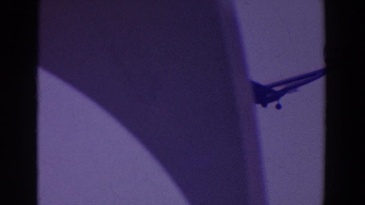 A silhouetted jet with landing gear appears near a vertical structure in purple-tinted 8mm footage from the reported 1964 fair clip.