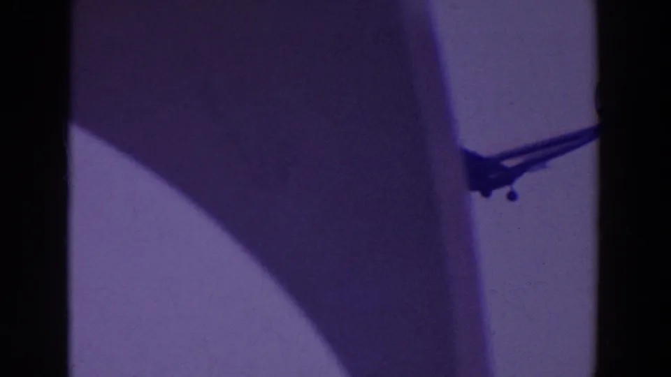 A silhouetted jet with landing gear appears near a vertical structure in purple-tinted 8mm footage from the reported 1964 fair clip.