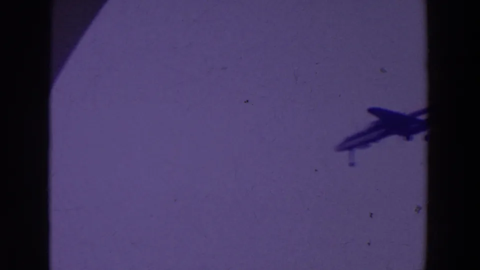 A small jet silhouette with visible landing gear crosses the purple sky in the archival home-movie footage.