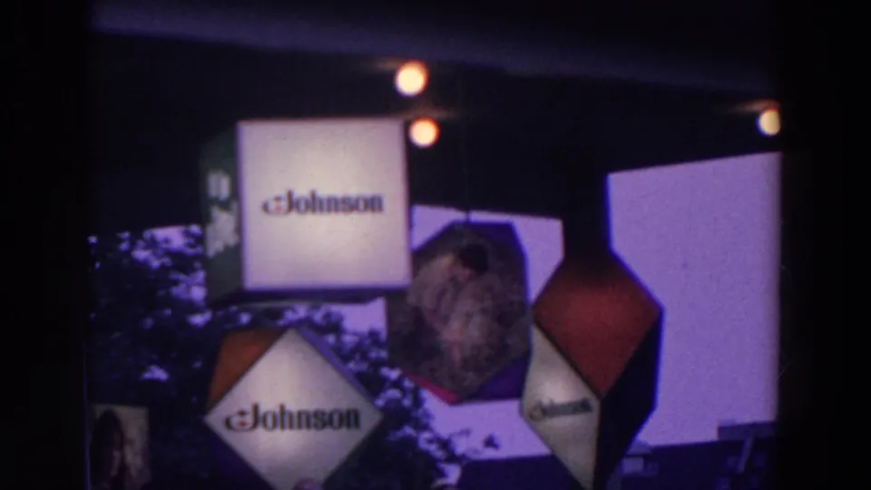 Johnson-branded display cubes and geometric hanging forms appear beneath a dark roofline in the fairground scene.