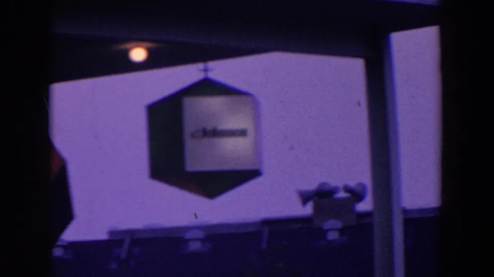 A Johnson-branded hanging cube is framed by dark posts and a roofline in the purple-tinted fairground footage.