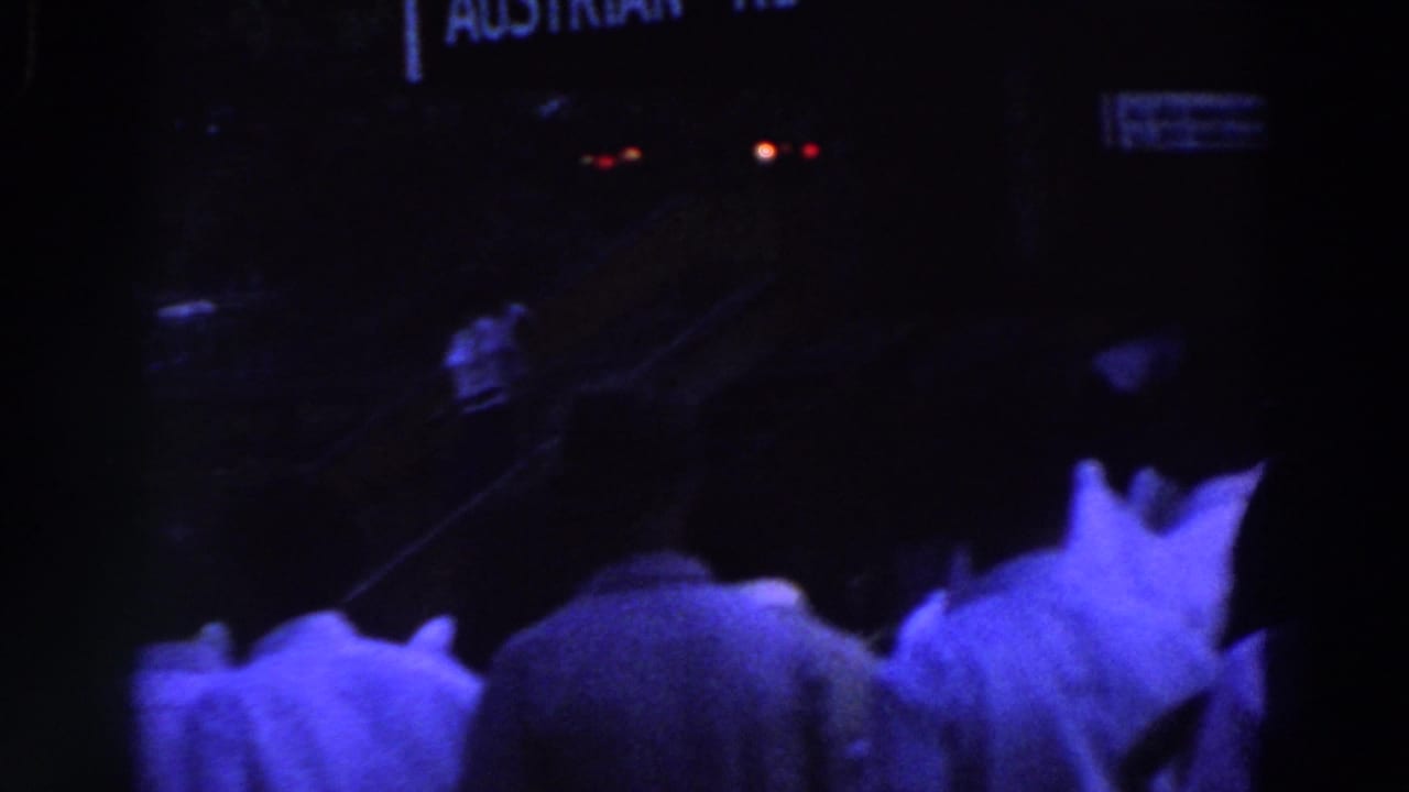 Visitor-shot 8mm frame from the 1964 World's Fair showing a dim crowd near partial Austrian Restaurant signage.