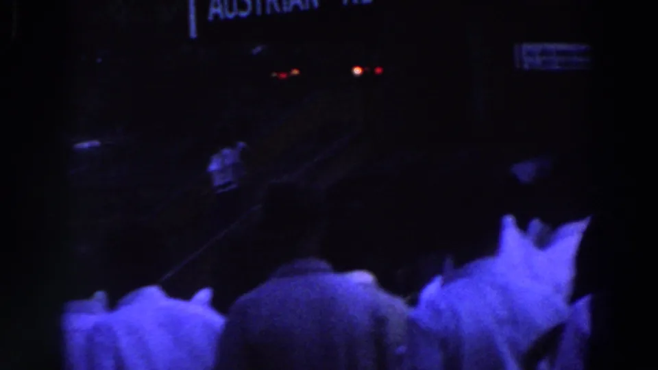 Visitor-shot 8mm frame from the 1964 World's Fair showing a dim crowd near partial Austrian Restaurant signage.
