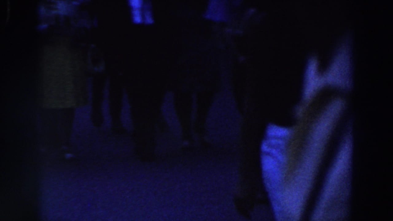 Dark blue-tinted scene with shadowed figures and legs barely visible.