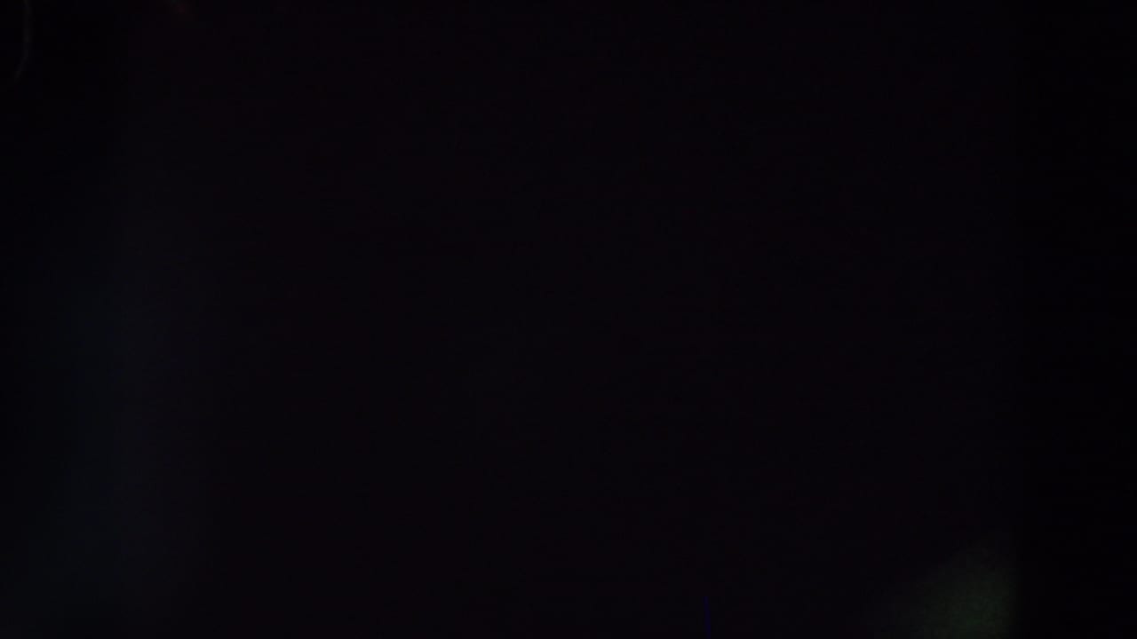 Dark 8mm frame with faint vertical structures and no identifiable people, signage, or location detail visible.