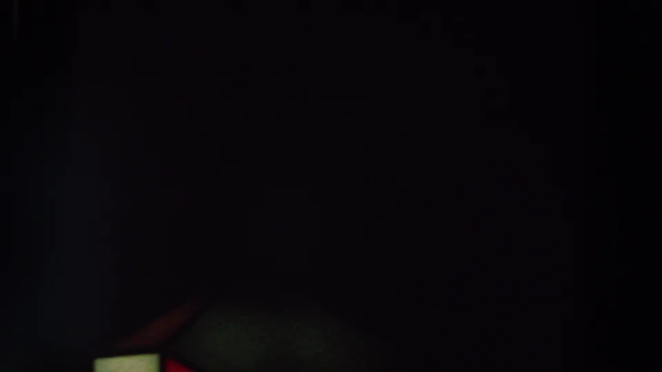 Low-light 8mm frame showing partial red and green geometric forms near the bottom, with surrounding detail obscured by shadow.