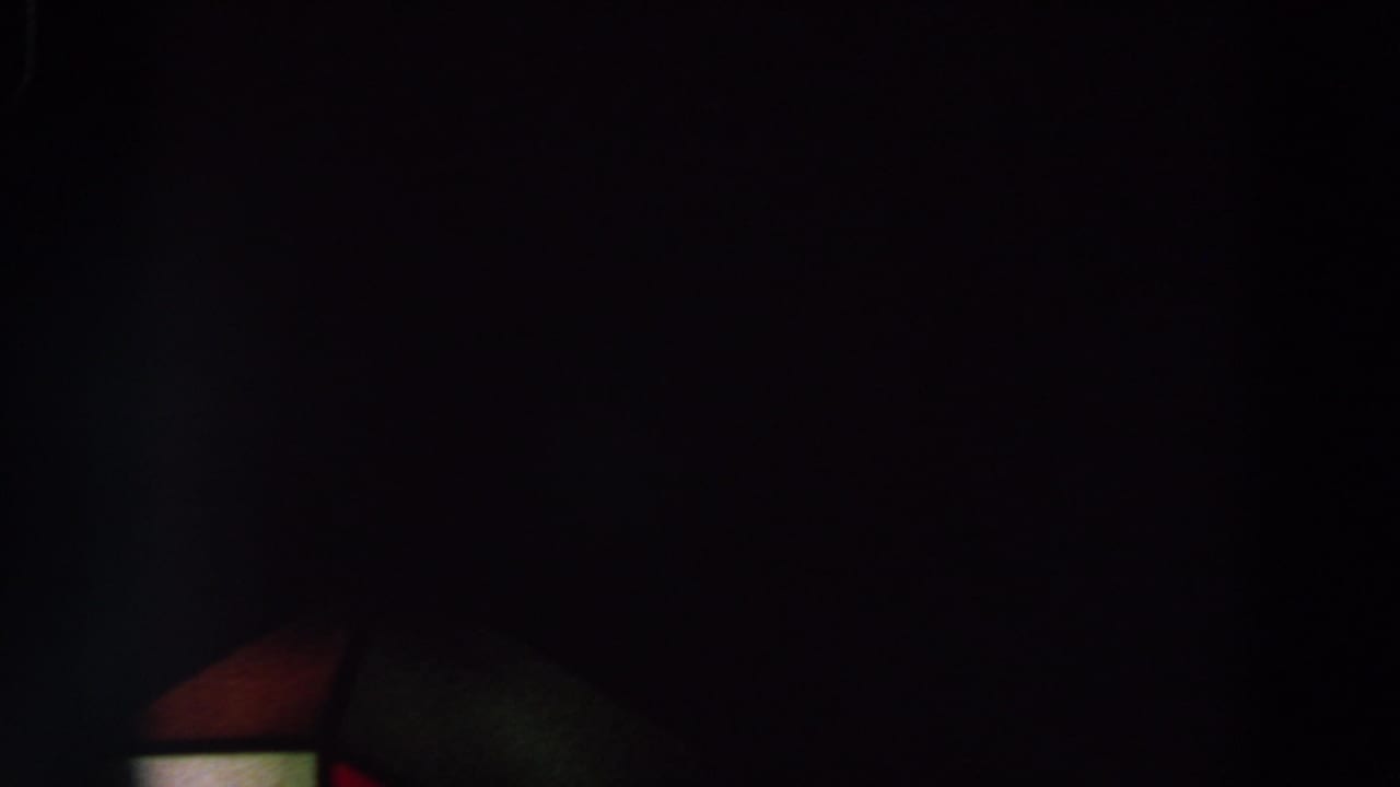Underexposed 8mm frame with a mostly black sky, faint colored structure edge, and tiny orange lights, metadata associated with 1964 World's Fair footage.