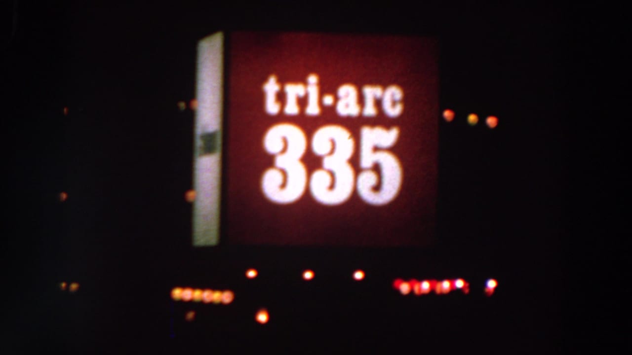 Red Tri-Arc 335 sign glowing in darkness with scattered small lights nearby.