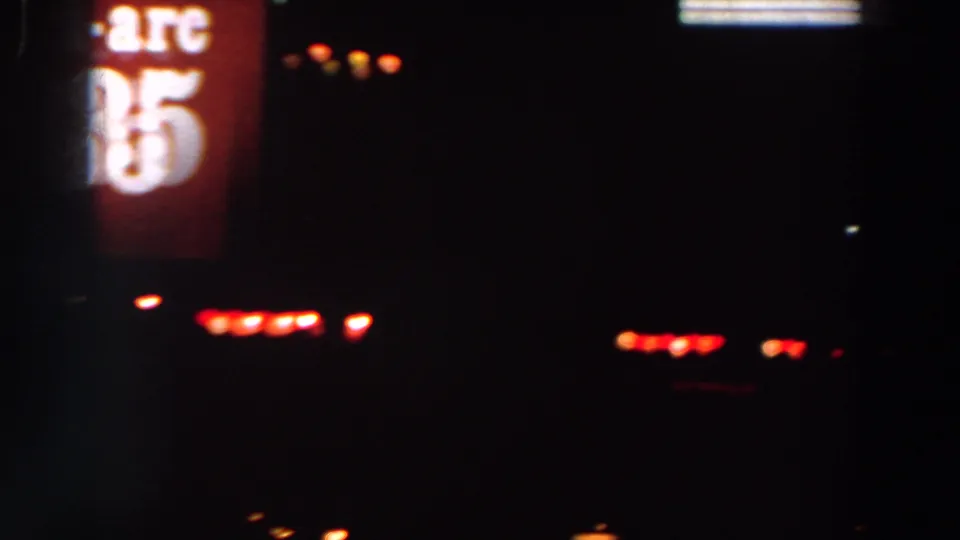The camera catches part of a red Tri-Arc 335 sign at night, with blurred red and white points of light across the darkness.