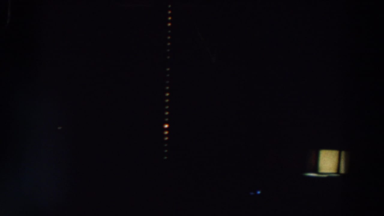 Very dark night frame with faint building shapes and a vertical row of small warm lights.