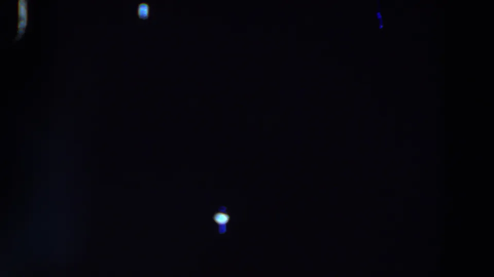 Mostly black 8mm frame with a brighter blue-white light spot near the lower right and faint flare in the surrounding darkness.