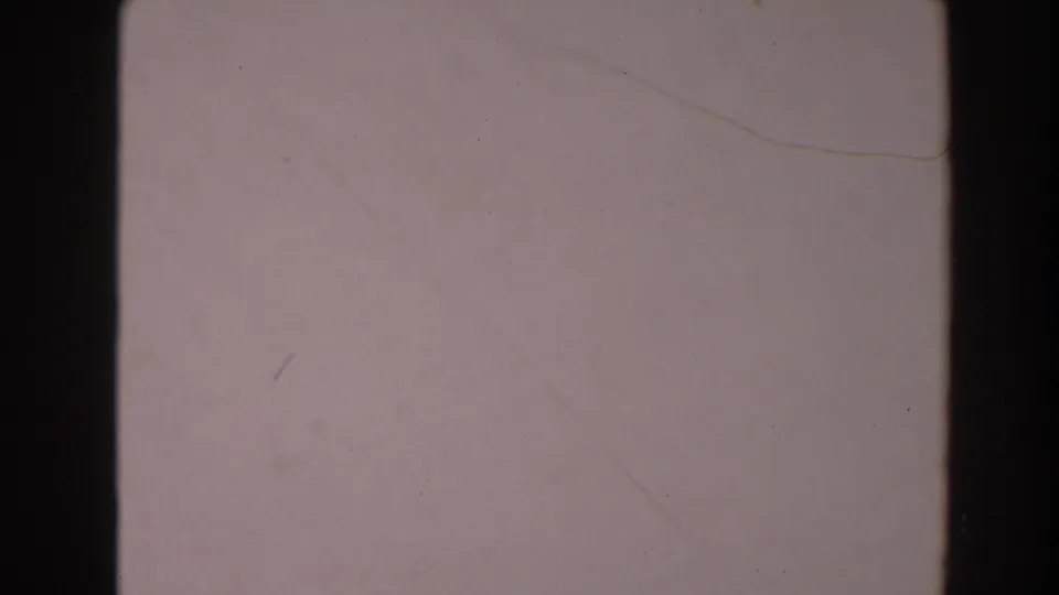 1964 North Hollywood 8mm frame of a pale concrete surface, bordered by dark film edges with faint scratches and dust.