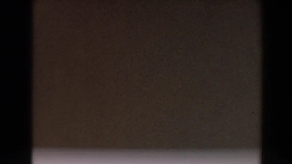 1964 North Hollywood 8mm frame showing a darker ground surface beneath pale concrete, with grain and vertical frame borders.
