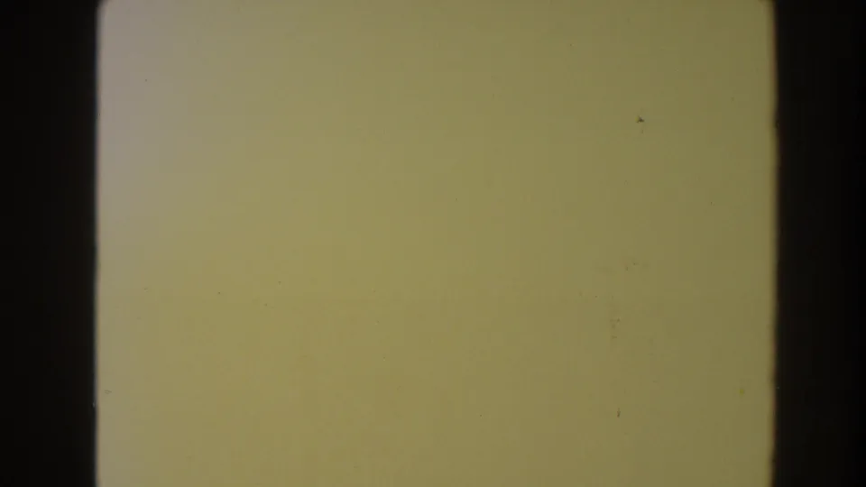 1964 North Hollywood 8mm frame of a yellow-tinted concrete or pavement surface with dust, grain, and dark frame edges.