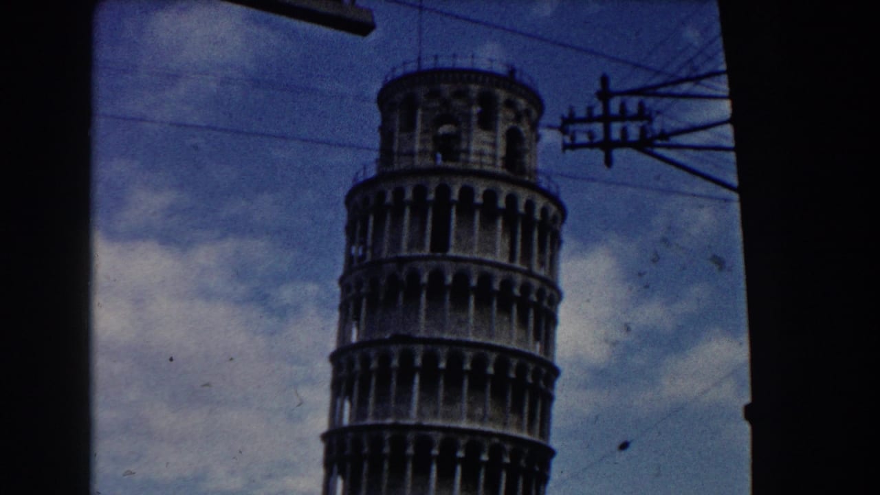 1959 8mm view of the Leaning Tower of Pisa with overhead utility lines and a blue sky visible through the film frame.