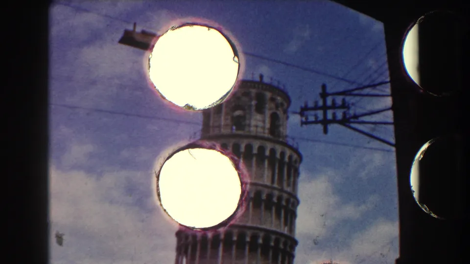 1959 8mm Pisa frame with the Leaning Tower partly hidden by bright film damage or exposure spots and overhead wires.