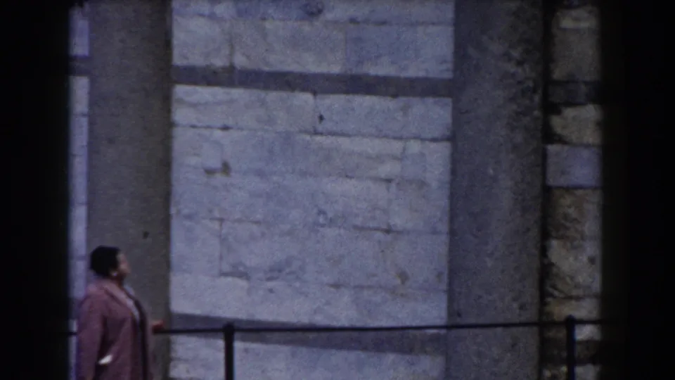 A partial frame shows the woman in a pink coat near the black railing, with the Leaning Tower's pale stonework filling the background.
