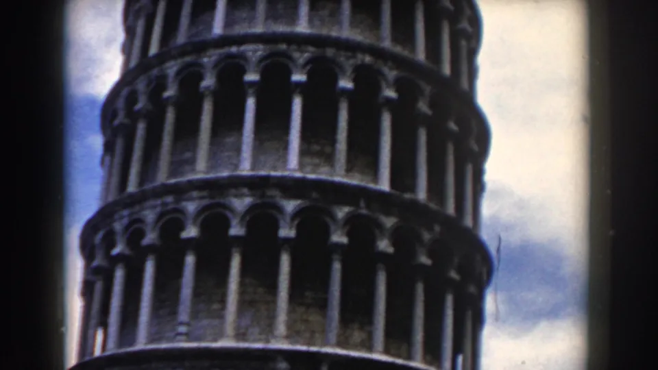 1959 Pisa frame showing the upper tower levels, repeated columns, and pale blue sky with clouds.