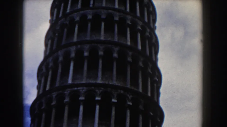 1959 Pisa frame showing the tower's stacked arcaded levels in soft, grainy color against cloudy sky.
