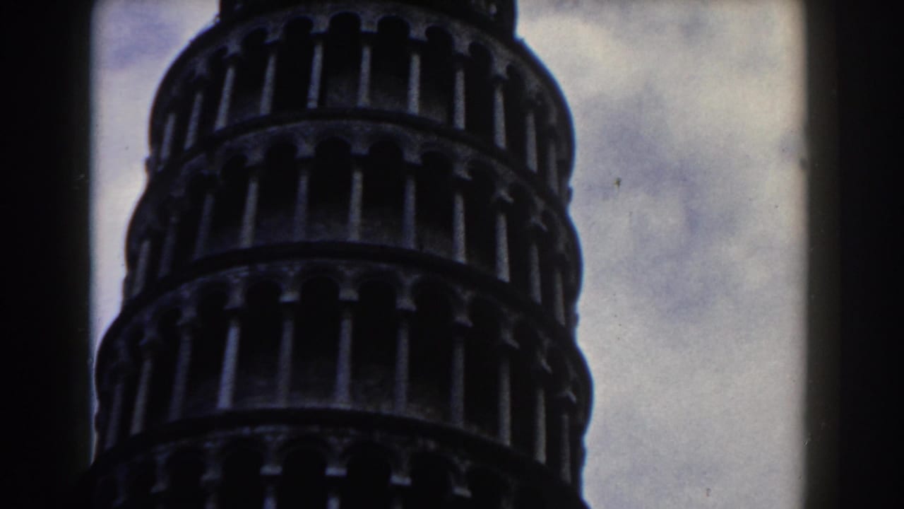 1959 8mm low-angle view of the Leaning Tower of Pisa, with arched galleries silhouetted against a cloudy sky.