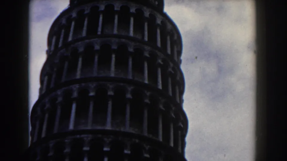1959 8mm low-angle view of the Leaning Tower of Pisa, with arched galleries silhouetted against a cloudy sky.