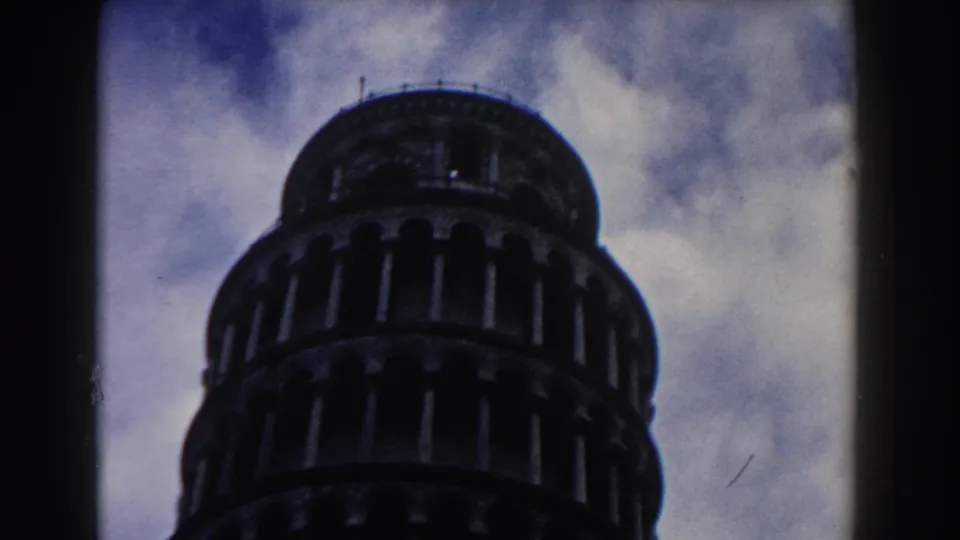 1959 home-movie frame from Pisa showing the upper Leaning Tower against bright clouds, with visible film grain and borders.