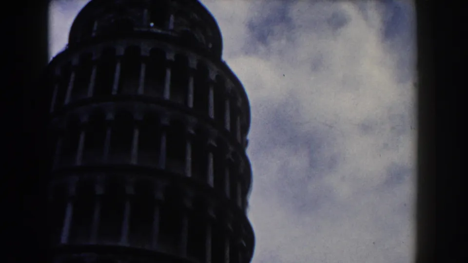Low-angle 1959 Pisa frame with the Leaning Tower's arched tiers in shadow and cloudy sky visible around the structure.