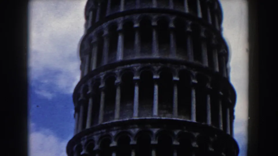 The Leaning Tower of Pisa appears in a close, dark-edged 8mm frame with blue sky and clouds behind it.