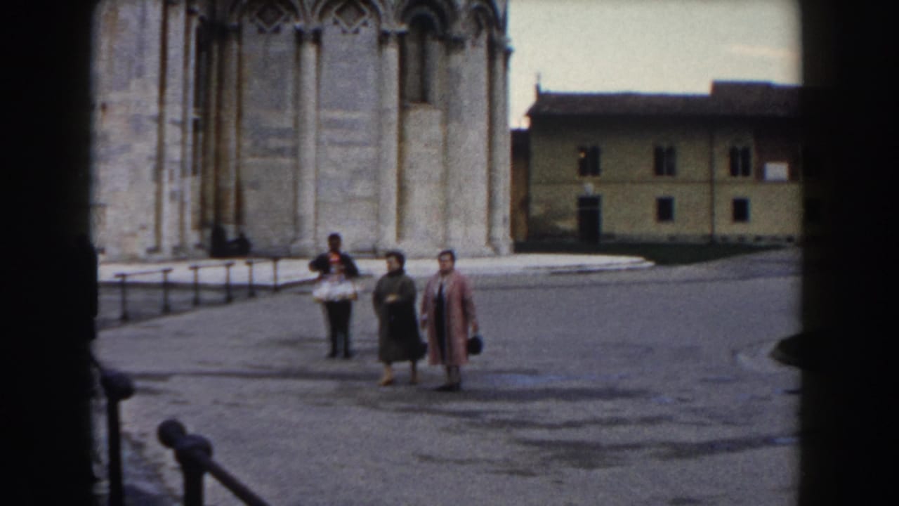 Two women and a man walk across a paved square beside a large stone cathedral facade.