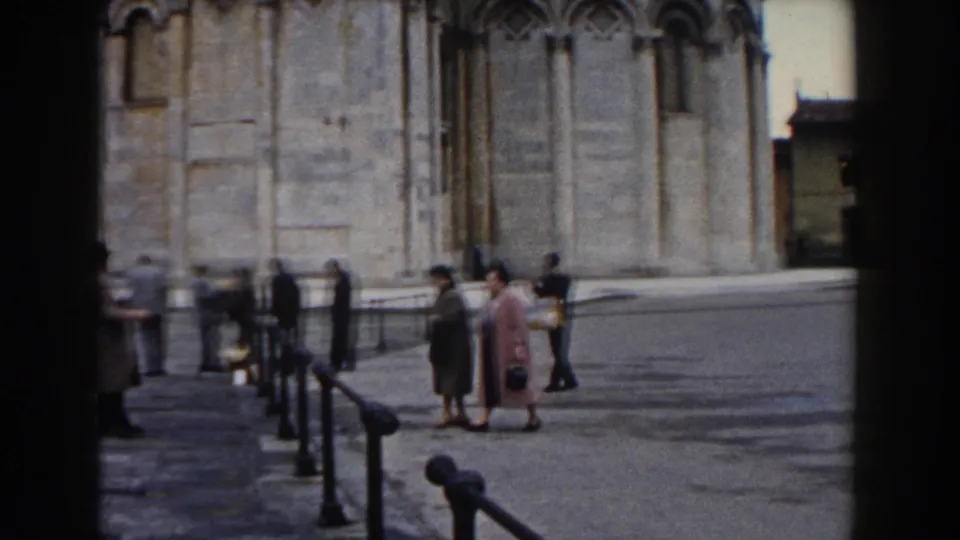 The women remain near the railings in Pisa’s piazza as other visitors pass along the cathedral facade.