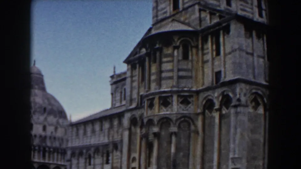 1959 8mm frame of Pisa Cathedral's corner structure with arches and a distant baptistery dome at left.
