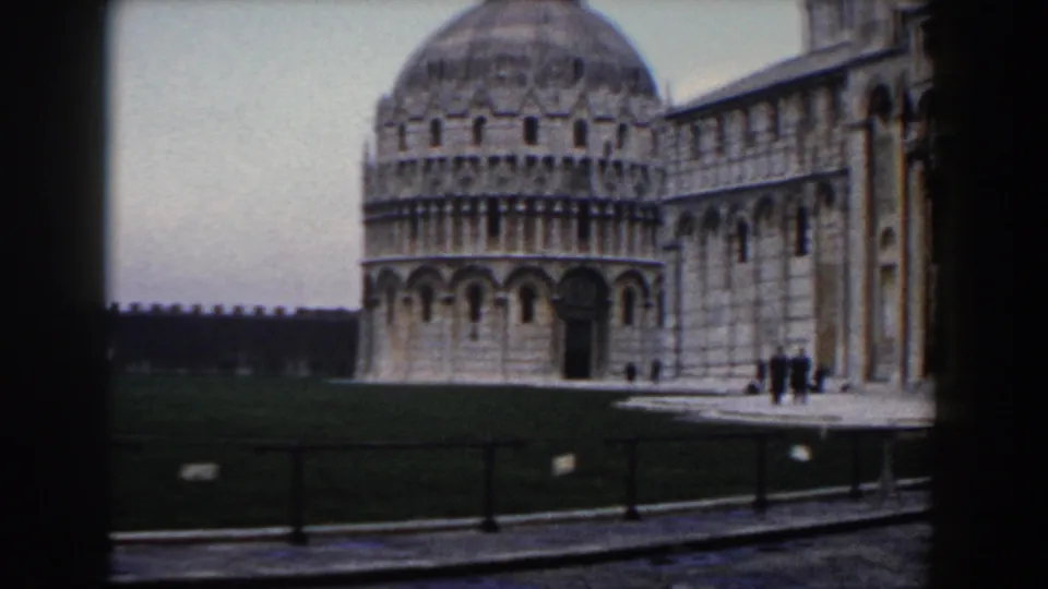 1959 Pisa view of the Baptistery and Cathedral across the grass, with several distant people walking near the building.