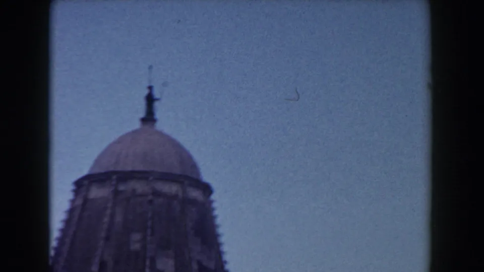 Handheld 1959 Pisa footage frames the upper dome of a landmark building against a clear blue sky.