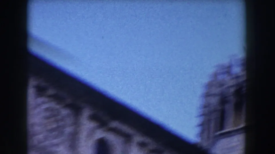 1959 Pisa cathedral exterior view with blue sky, roofline, and a partial stone tower or facade edge at the right.