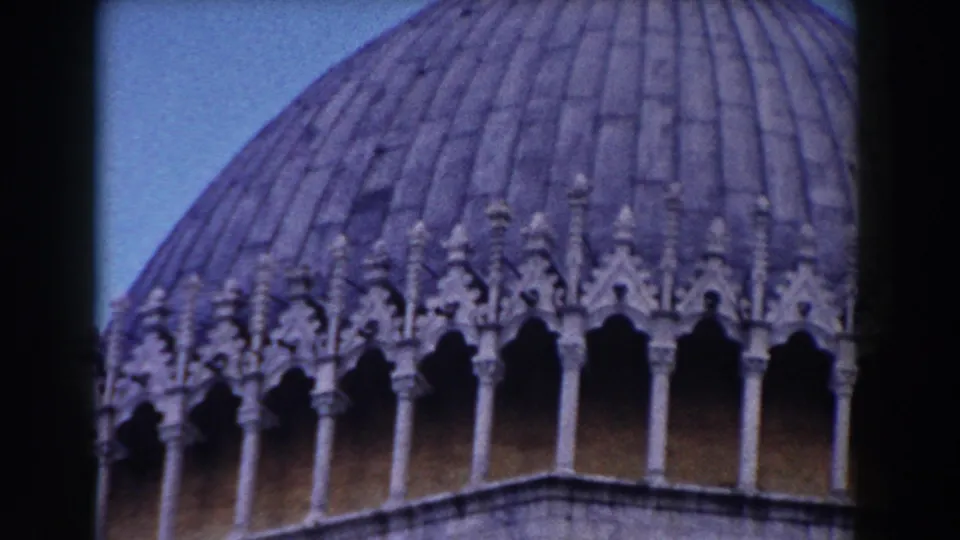 1959 Pisa church exterior detail with ribbed dome, arched stone decoration, and blue sky in a home-movie frame.