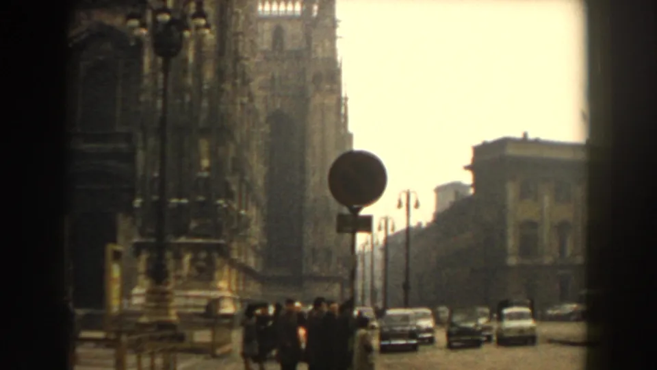 Wider view of a cathedral-side street with mid-century cars and signs in Italian footage cataloged as Pisa, 1959.