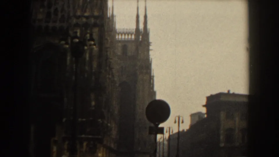 Hazy view of a large Gothic cathedral facade and nearby street sign in cataloged 1959 Italy travel footage.