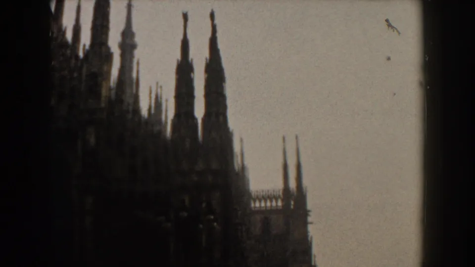 Italian 1959 home-movie view of ornate Gothic spires and roofline details seen through a window divider.