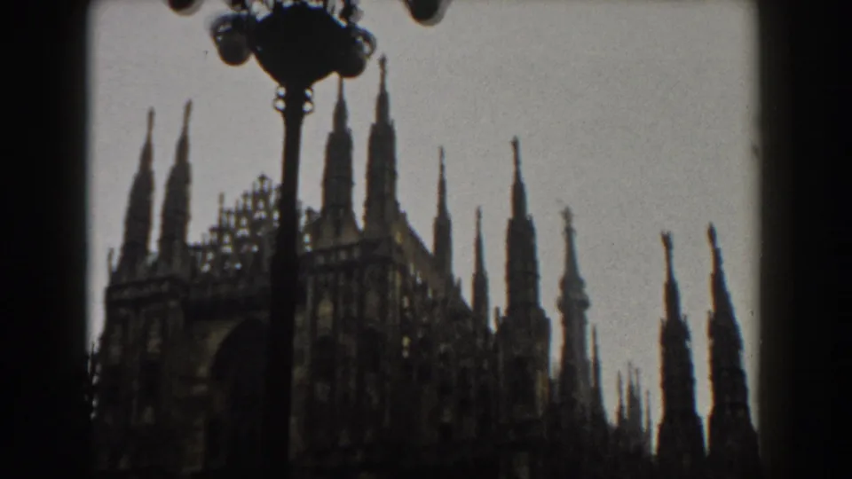1959 Italy home-movie frame showing Gothic cathedral spires with a dark streetlamp silhouette and window framing.