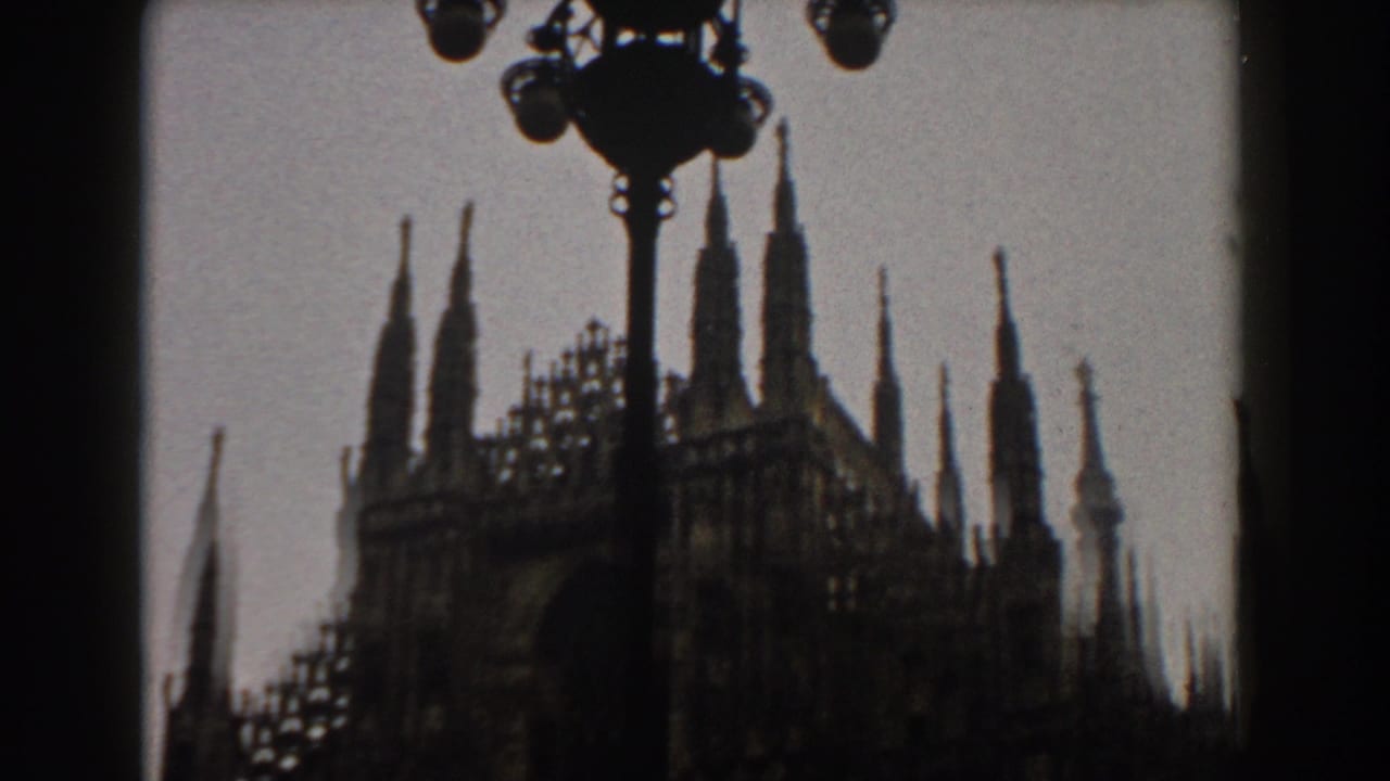 1959 8mm travel frame showing a Gothic cathedral facade in silhouette, likely Milan's Duomo, partly blocked by dark foreground shapes.