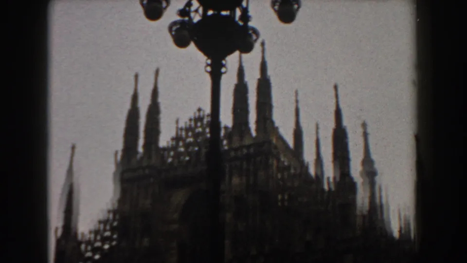 1959 8mm travel frame showing a Gothic cathedral facade in silhouette, likely Milan's Duomo, partly blocked by dark foreground shapes.