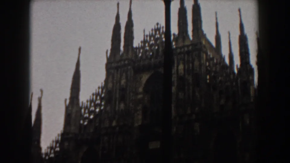 1959 8mm frame of an ornate cathedral exterior, likely Milan's Duomo, with spires and facade partly obscured by a dark vertical edge.