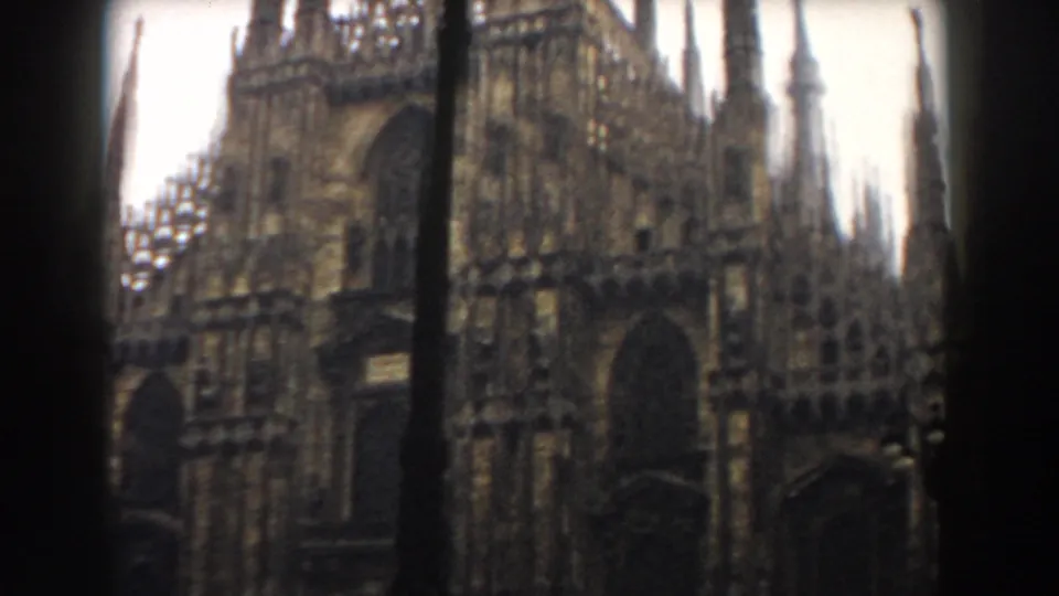 1959 color 8mm view of a Gothic cathedral exterior, likely Milan's Duomo, with detailed stonework and a dark pole crossing the frame.